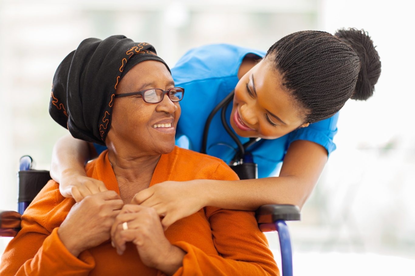 A caregiver cheerfully interacts with an elderly woman in a wheelchair.