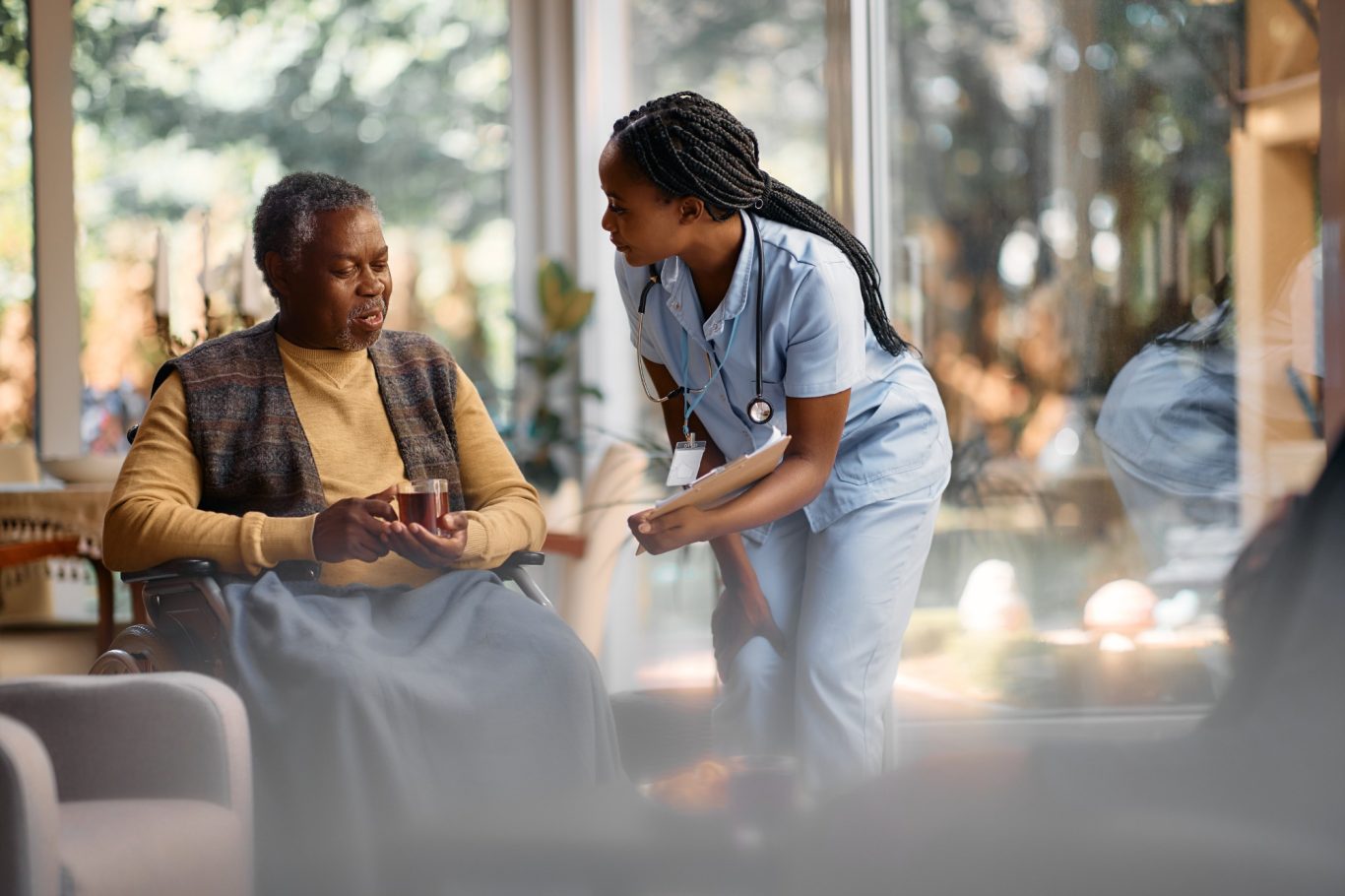Caregiver talking to a senior man in a cozy, sunlit room.